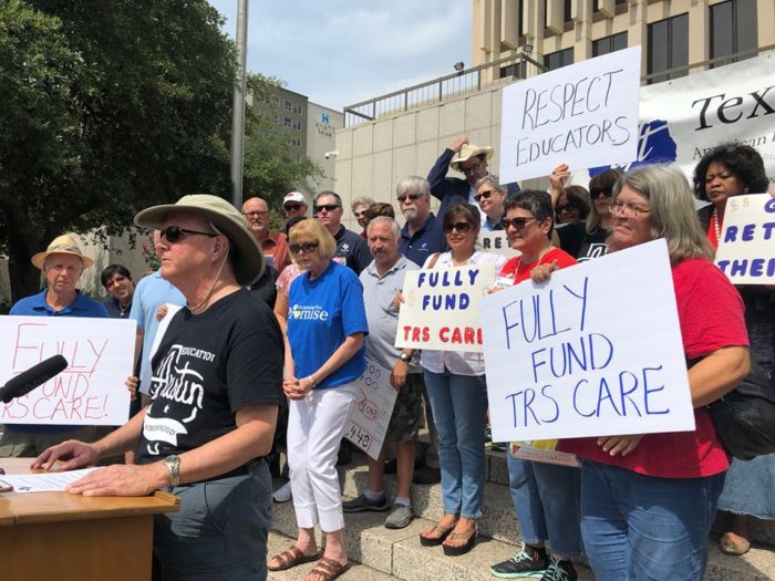A group of people gathered on the steps of the Texas Capitol holding signs advocating to fully fund retiree healthcare