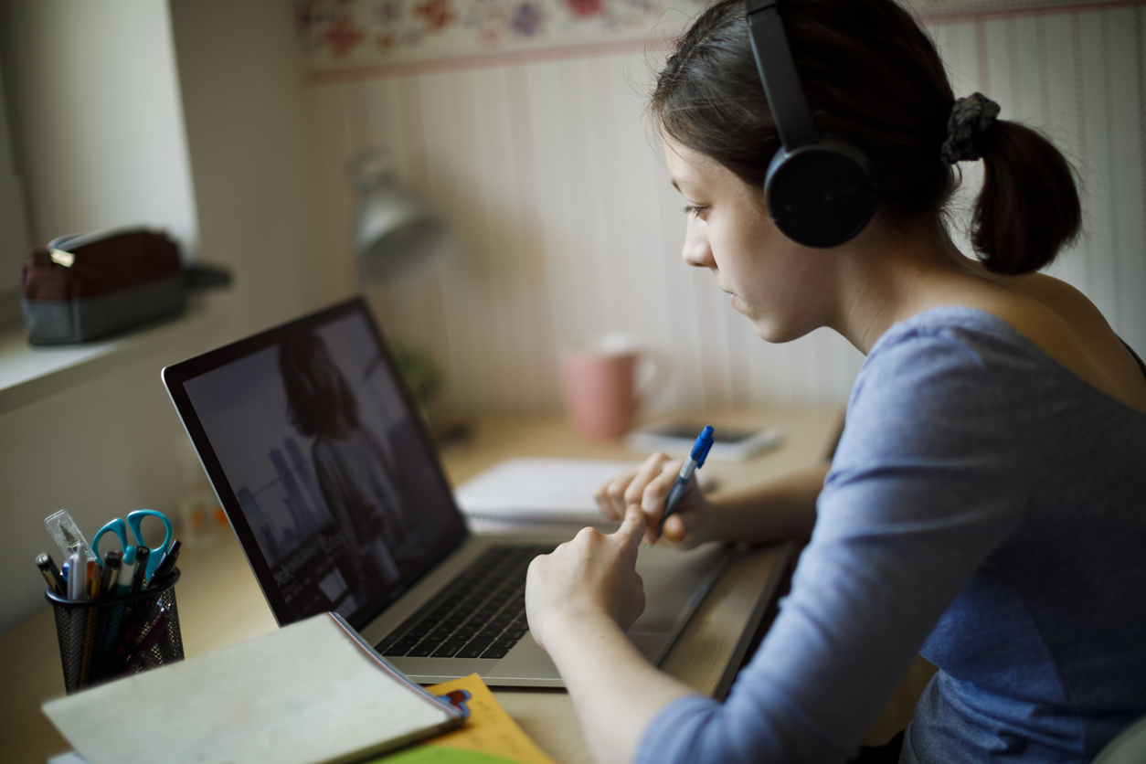Person sits at a desk with headphones, looking at a laptop.