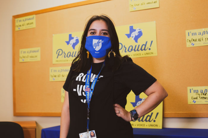 Mariah Najmuddin poses with hand on hip and an A-F-T face mask in front of a corkboard with yellow "Texas A-F-T Proud" signs.
