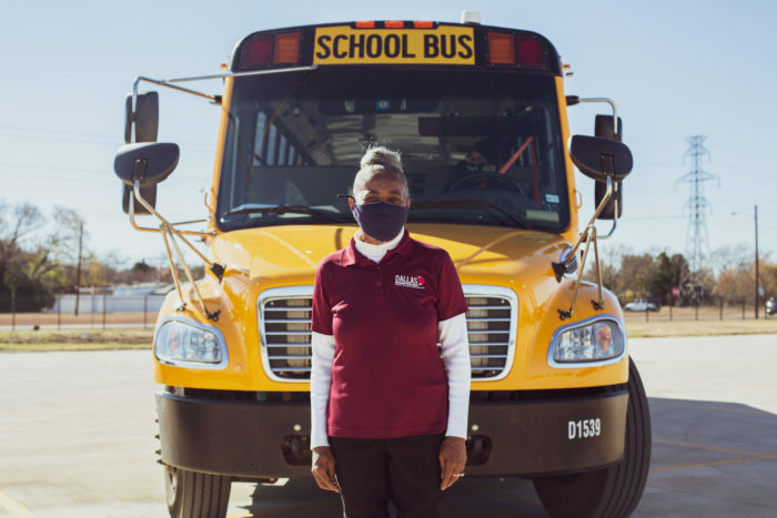Linda Barrett stands in front of a school bus wearing a face mask and her driver's uniform.