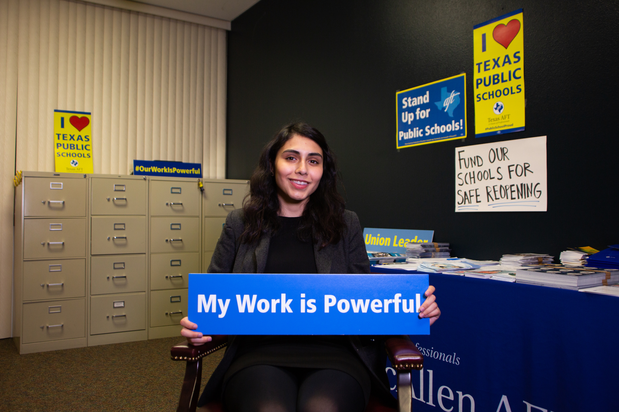 Clarissa Riojas, seated, holds a blue sign that says "My Work Is Powerful"