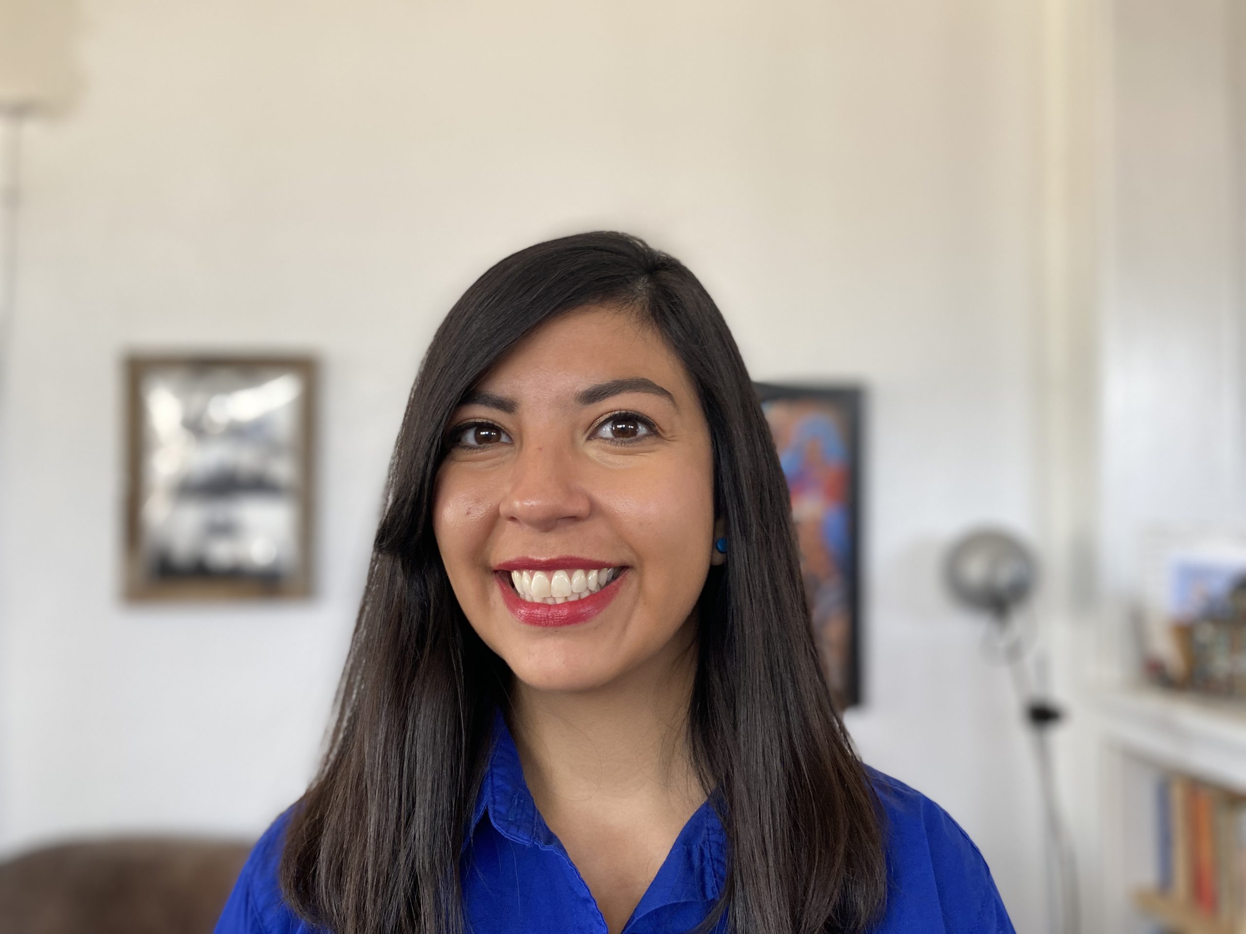 Alejandra Lopez, picture from shoulders up. In the background are framed photos on a wall.