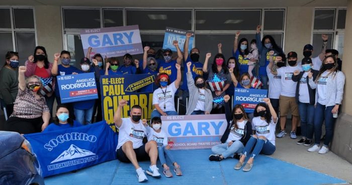 Socorro A-F-T members and allies pose for a photo outside a building. Everyone is wearing face masks and some are holding signs for endorsed school board candidates.